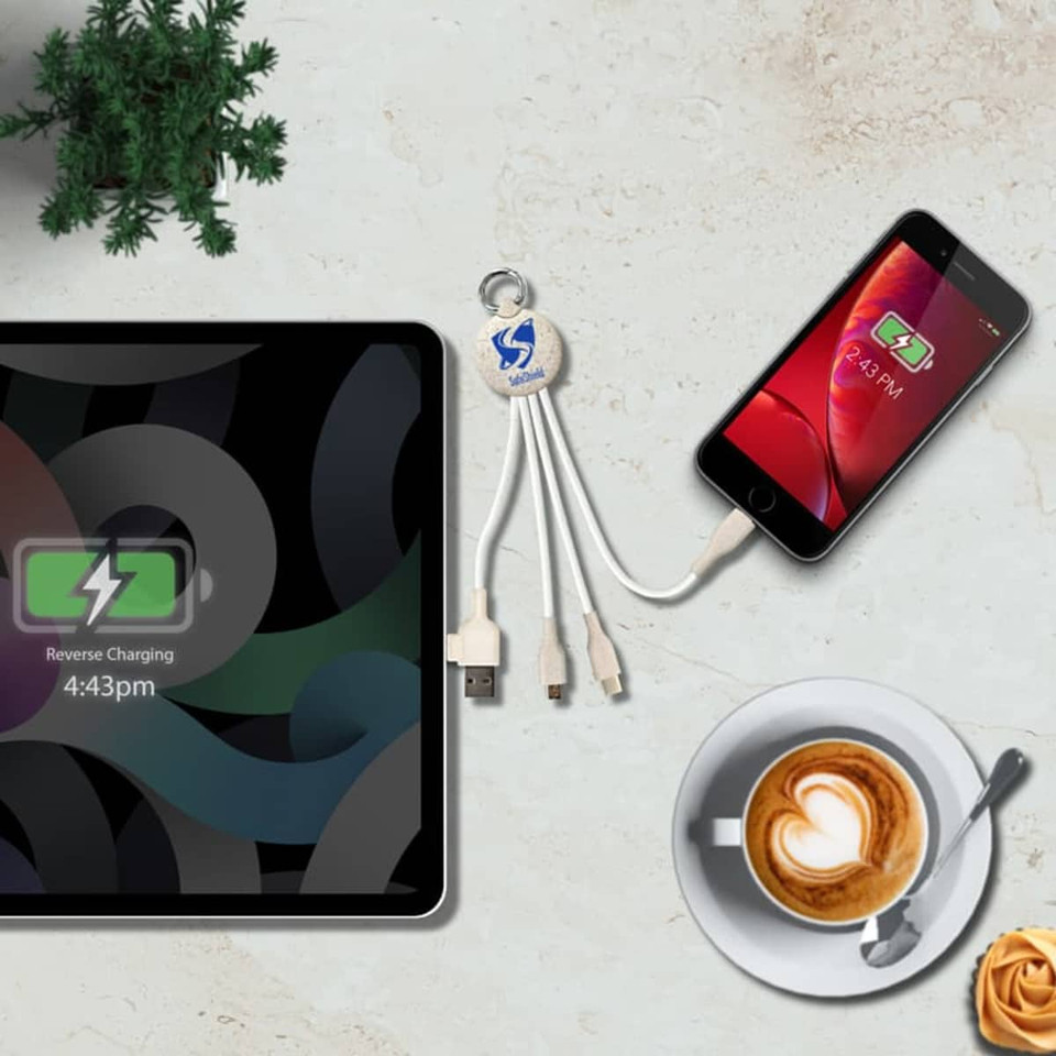 A wheat straw charging cable in white, connected to a phone and a tablet, on a marble tabletop with a coffee cup.