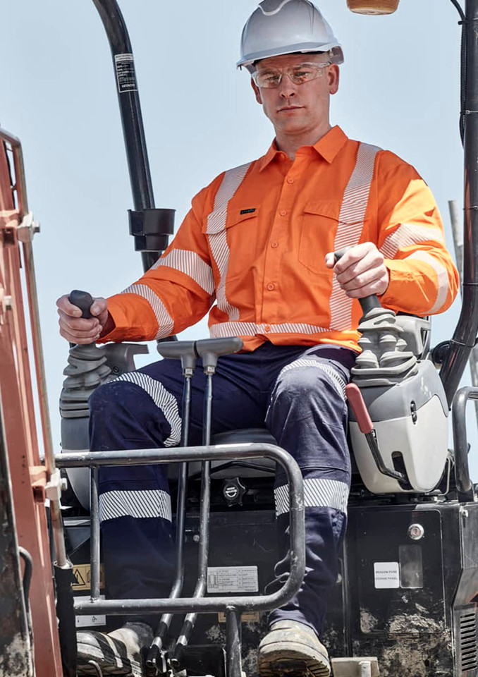 A man operates machinery wearing an orange Hi Vis shirt with segmented tape, alongside navy pants and a white hard hat.