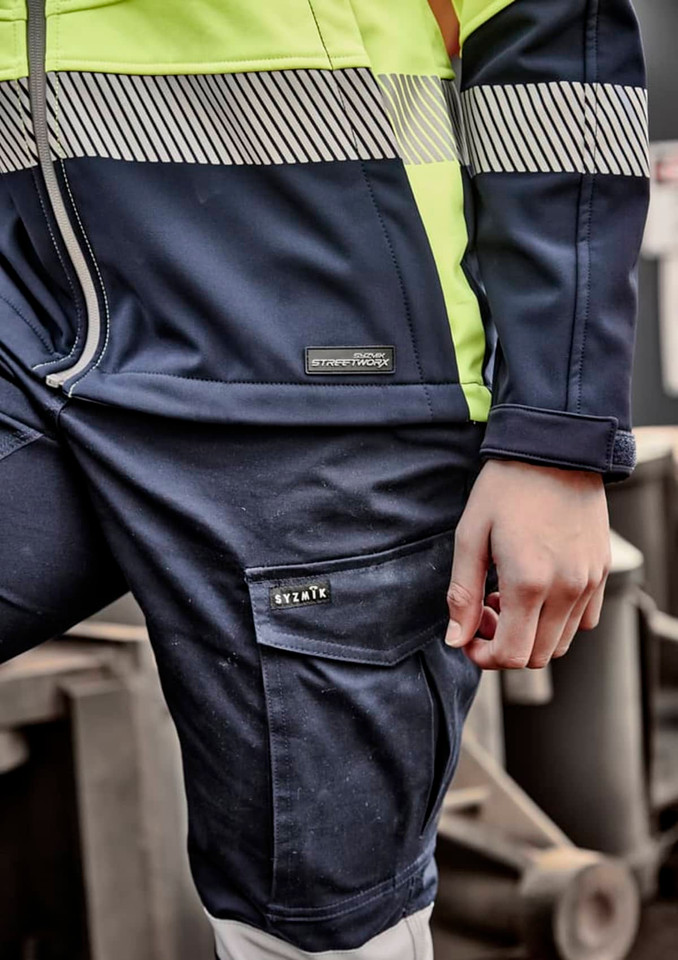 A close-up of a navy and high-visibility yellow softshell work jacket featuring a logo on the left chest and striped detailing.