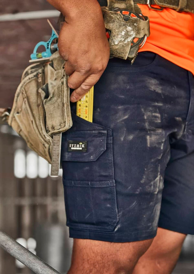 Men's navy cargo shorts featuring multiple pockets, worn with a tool belt, showing a measuring tape and work environment dust.