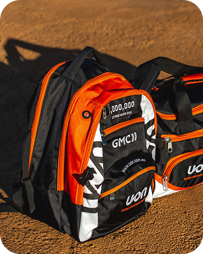 Two bags on sandy ground; a vibrant orange and black backpack, and a matching duffel bag