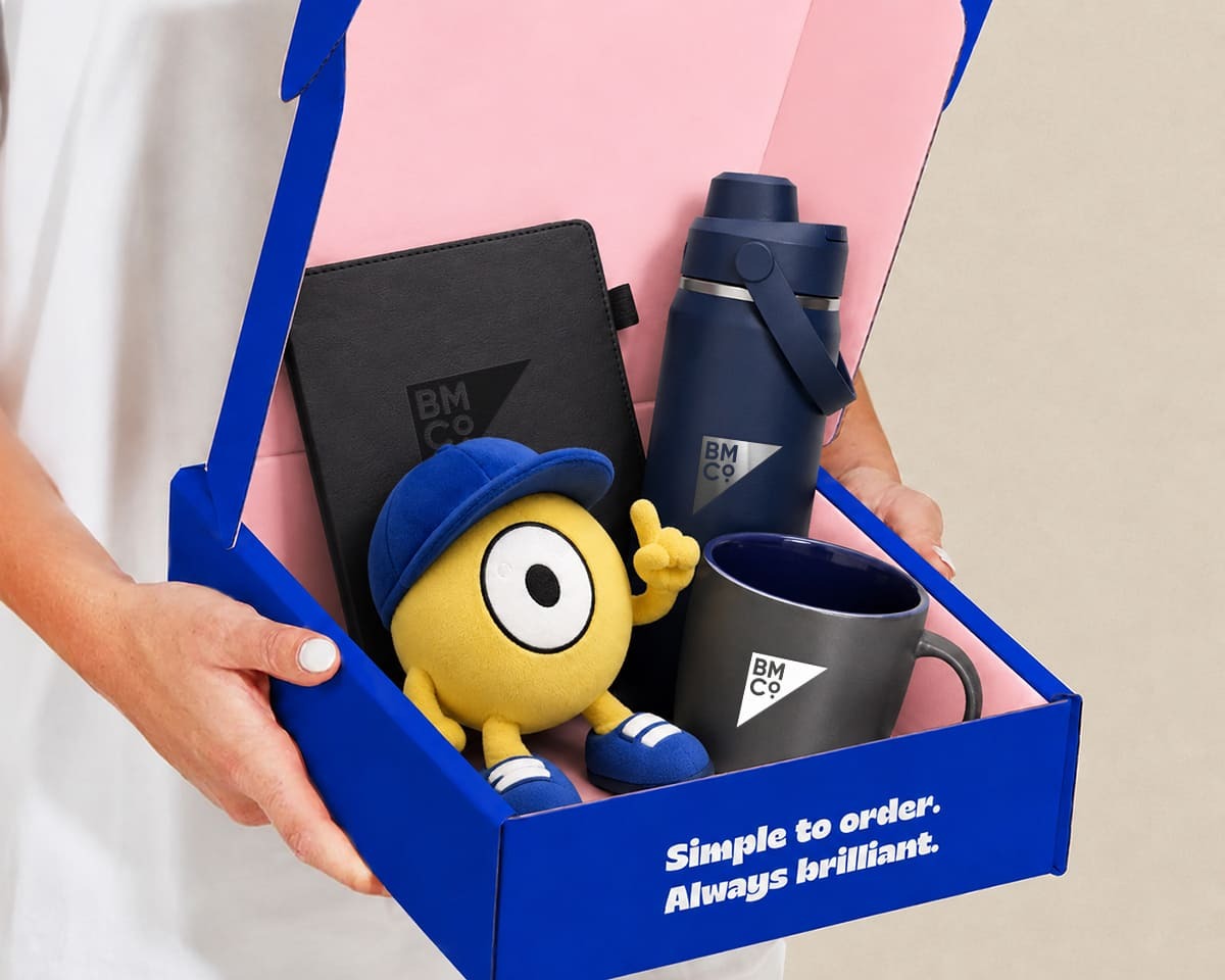 A person holding a welcome pack containing a bottle, notebook, mug and plush toy