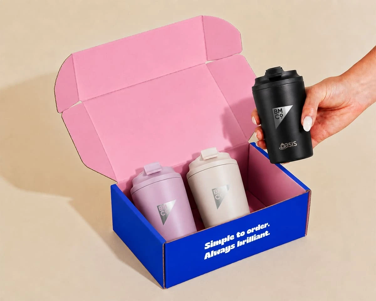 A box containing two coloured Oasis tumblers and a woman holding a black tumbler