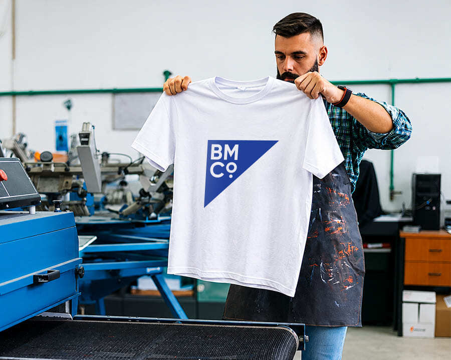 A man holding up a white tshirt with the Brilliant Merch Co logo screen printed on