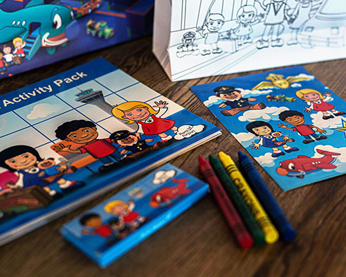 Children’s activity packs with cartoon characters, crayons, and colouring pages are arranged on a wooden surface
