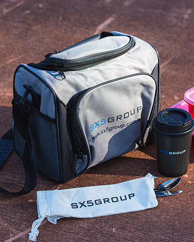 A gray and black insulated lunch bag labeled with a matching travel mug and cutlery set