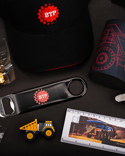 A collection of branded BTP merchandise including a hat, popcorn, can cooler, bottle opener, bandage, toy truck, and a ruler with construction-themed graphics