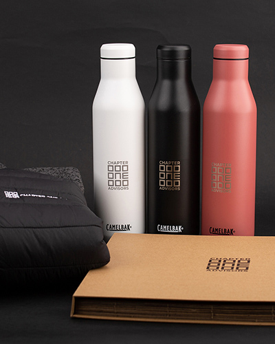 Three branded bottles in white, black, and red stand upright on a black surface