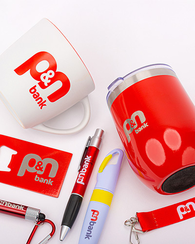 A collection of p&n bank-branded promotional items including a red tumbler, mug, pen, flashlight, lanyard, and bottle opener