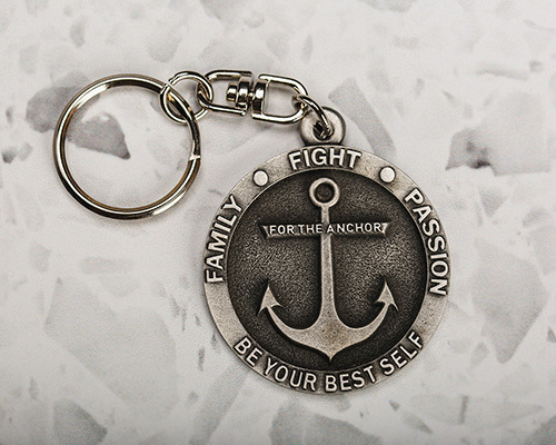 A round metal keychain features an engraved anchor
