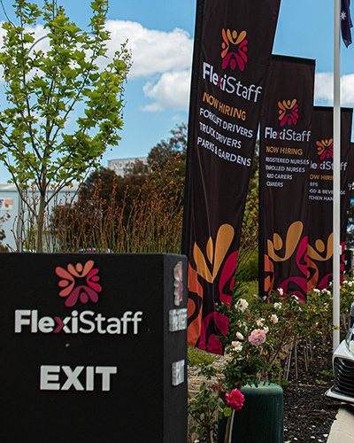 Flexistaff hiring banners outside with nearby flowers and trees under a blue sky