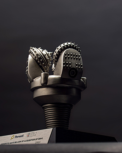 A metallic, intricately designed drill bit displayed on a stand against a dark background