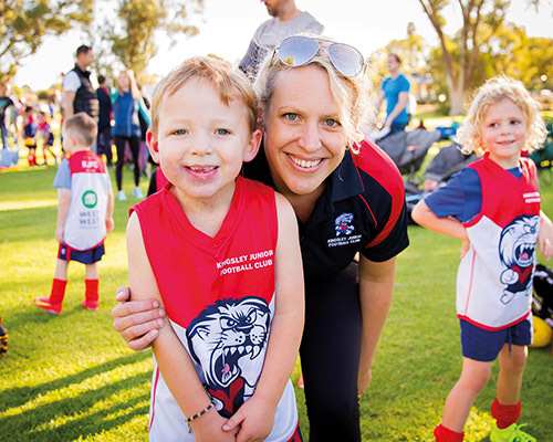 A smiling child in a red sports jersey and a woman in a matching shirt on a sunny field