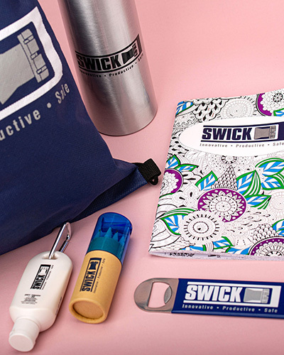 A collection of swick-branded products on a pink background, including a tote bag, water bottle and more