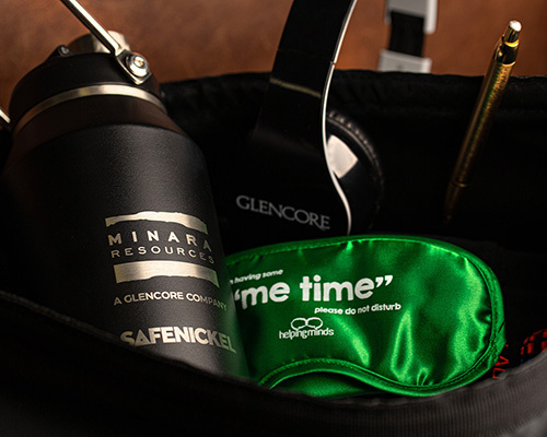 A black minara resources-branded water bottle, glencore-branded headphones, and a green sleep mask
