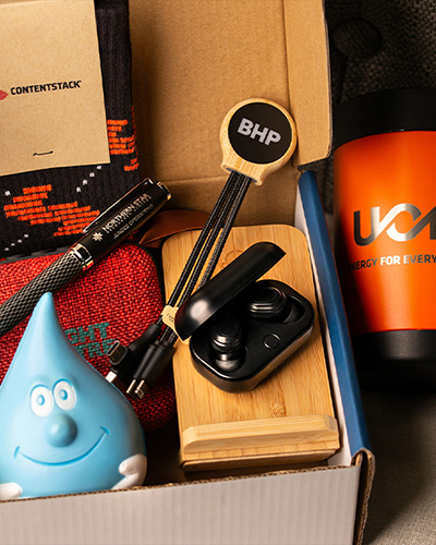A gift box with branded items: black and red socks, black pen, headphones, stress ball, keychain, and an orange mug
