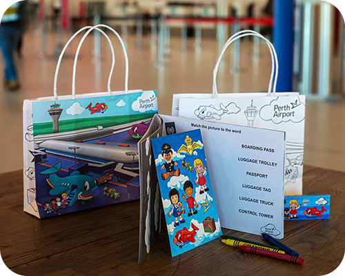 Two colourful perth airport gift bags sit on a table alongside an activity book