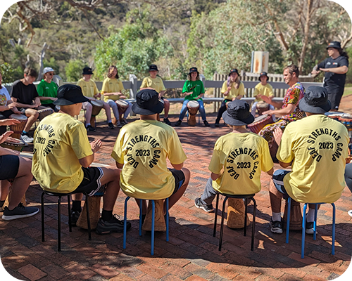 A group of young people in yellow shirts sit on stools forming a circle, outdoors
