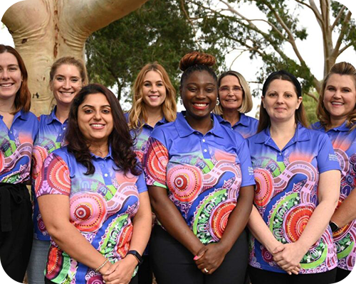 A diverse group of women stands outdoors, wear colourful, patterned shirts