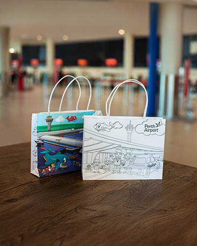 Two illustrated paper bags are on a wooden table at perth airport