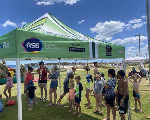 People chatting and enjoying themselves under a tent, with a sign hanging above them