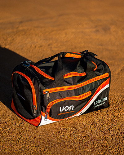 A black and orange sports duffel bag sits on a textured brown surface