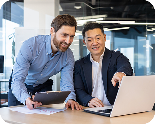 Two men in a modern office, one in a blue shirt and the other in a suit, smiling while working