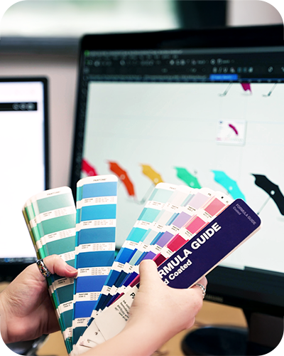 Hands holding colour swatches in front of a computer displaying a design with colourful umbrellas