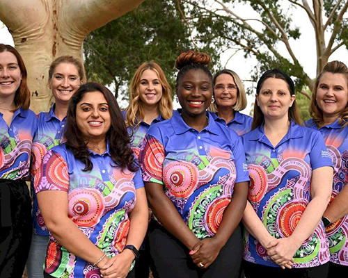 Team members smiling while wearing custom polo shirts with a beautiful, colourful Aboriginal art design