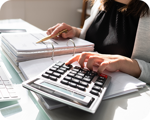 A person in business attire uses a calculator and reviews documents