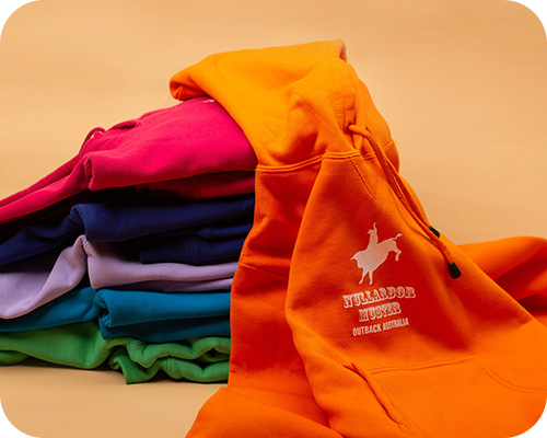A stack of nullarbor muster branded vibrant hoodies in orange, pink, blue, and green with an orange hoodie in front