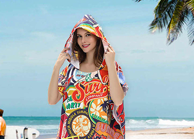 A woman wearing a colourful, patterned hooded cover-up smiles on a tropical beach
