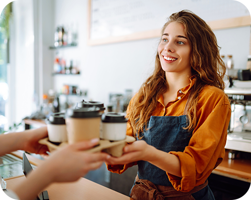 Smiling barista in a coffee shop hands a tray of takeaway coffee cups to a customer