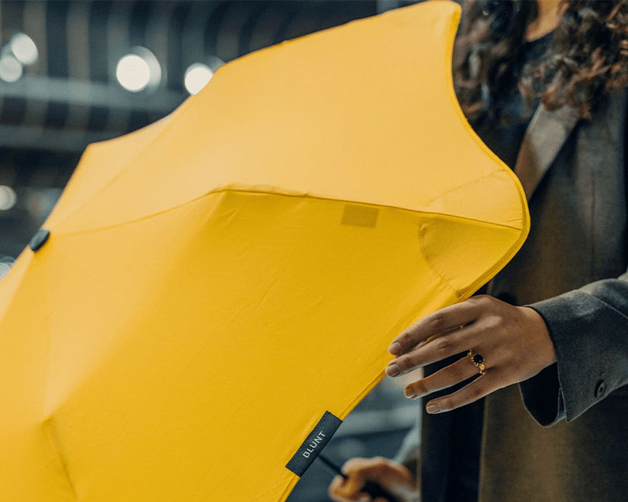 Woman holding out a yellow Blunt umbrella