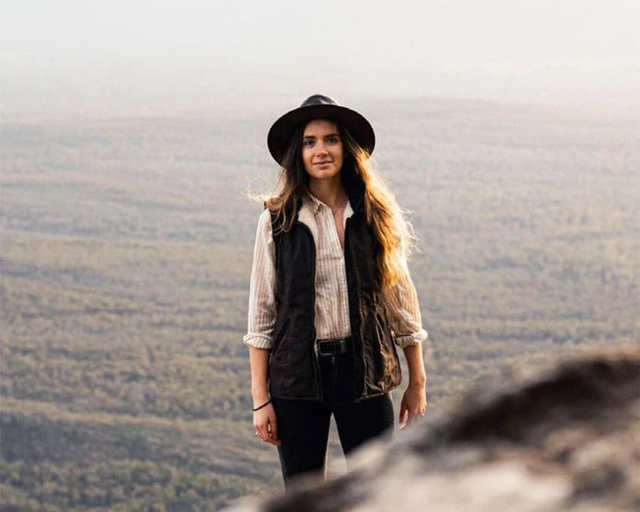 A woman standing on a mountain with a view behind her