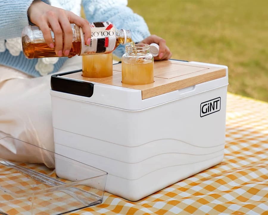A woman pouring a drink into a glass on a wooden cooler box