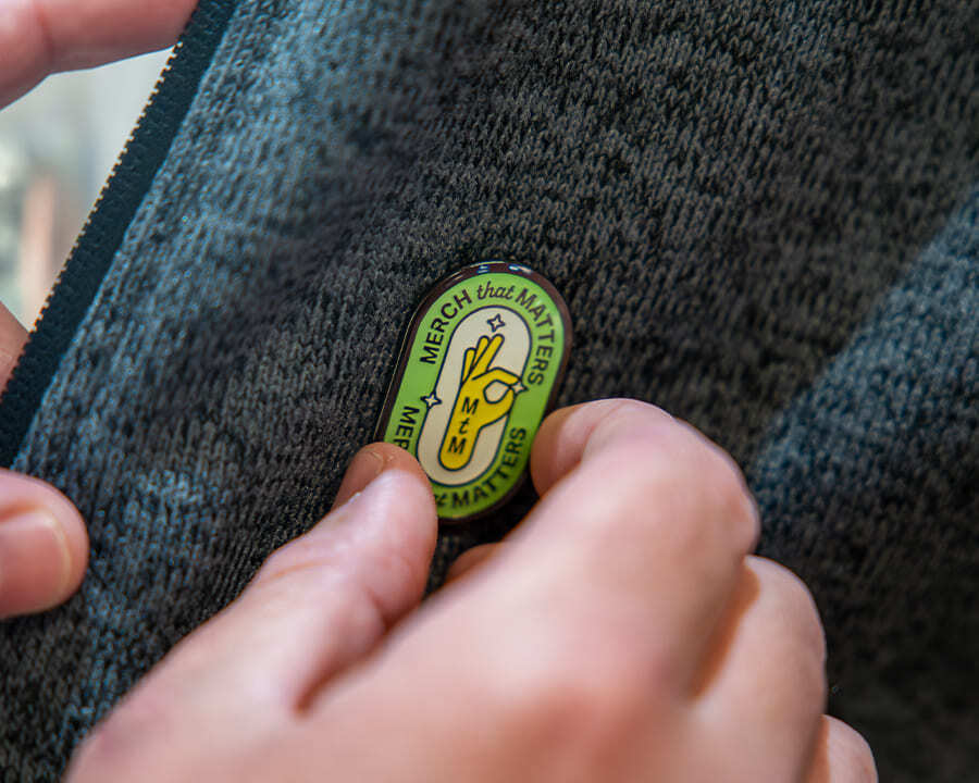 Close-up of a Look Brilliant Merch that Matters pin being placed on a jacket