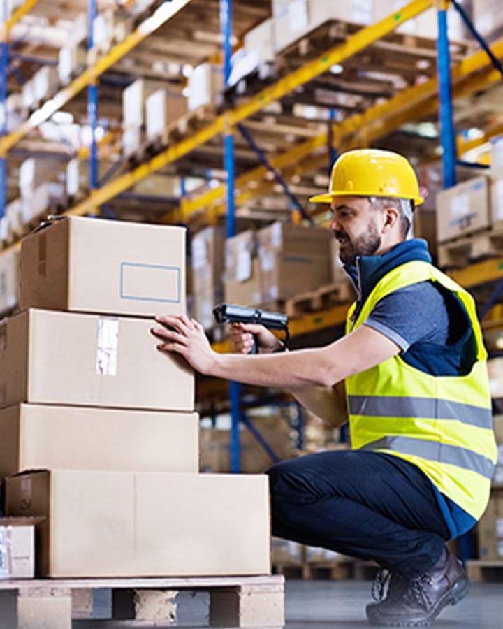 A man in a warehouse interacting with a stack of boxes