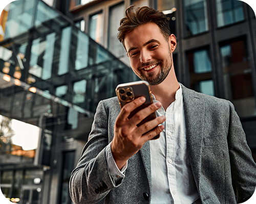 Young man in a grey blazer smiles while looking at his smartphone