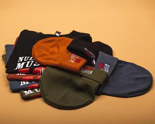 A collection of folded beanies in various colours, laid over printed t-shirts