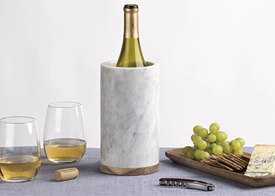 A wine bottle in a marble cooler next to two glasses of wine and a tray of food on a grey tablecloth