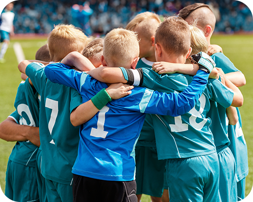 Young soccer team in teal and blue jerseys huddle with arms around each other