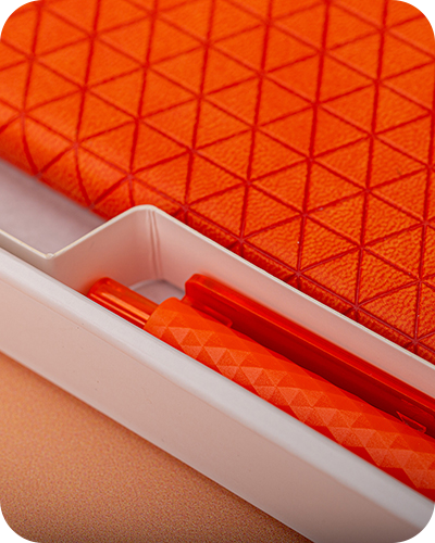 Close-up of an orange notebook with a geometric triangle pattern, paired with an orange pen