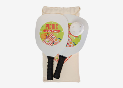Two white paddle rackets paired with a white ball, all placed on a beige bag