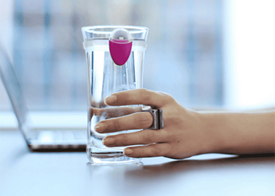 A hand with a smart ring lifts a glass of water beside a laptop