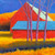 A square contemporary landscape oil painting by Peter Batchelder titled Amber Meadow, depicting brilliant red barns with a blue roof behind bare trees in a golden field under a dark blue sky.