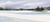 Wide horizontal panoramic watercolor painting of a small pine-covered island sitting in a frozen white lake under a gray winter sky by Mike Driscoll
