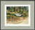 Horizontal watercolor painting of a white wooden dory boat with a wrapped orange sail pulled up onto a sandy and rocky shore in front of green trees by Mike Driscoll