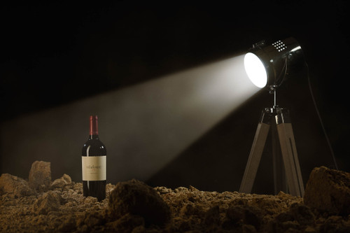 Bottle of Vilafonté Series M, Paarl 2013 red wine with dark fruit and oak. Bottle of wine standing in pile of stand, lit up by a set stage light on a tripod.