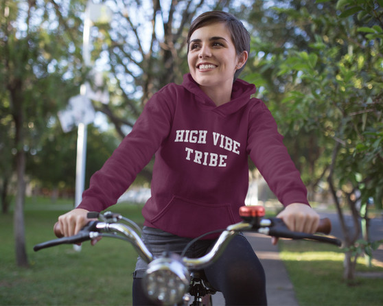 Young smiling woman with short hair riding a bicycle and wearing a maroon hoodie that has high vibe tribe printed on the front.